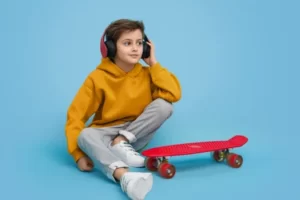 мальчик слушает музыку в наушниках и худи рядом с красным пеннибордом