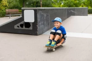 мальчик в синей футболка съехал сидя на скейтборде в скейтпарке Skate Scool