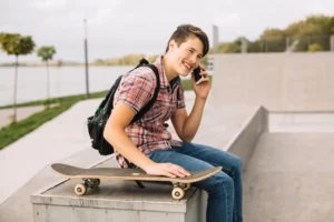 школа скейтбординга взрослый подросток сидит со смартфоном с улыбкой довольной Skate Scool